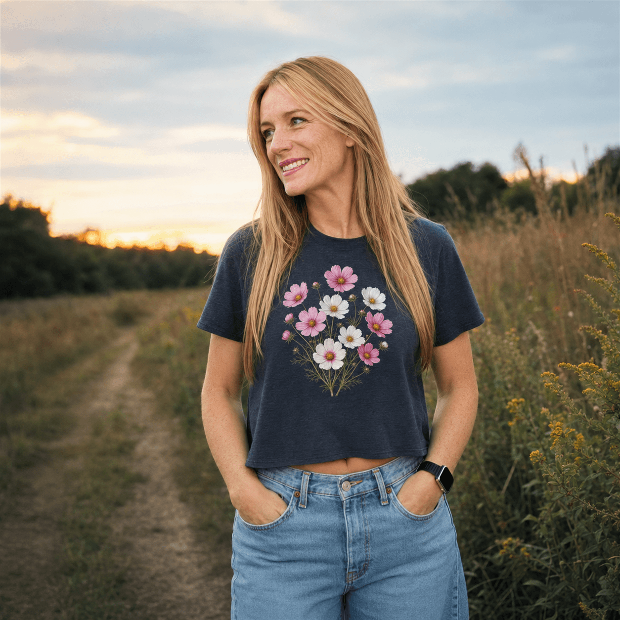 A woman in a dark floral tee and jeans stands outdoors in evening light.